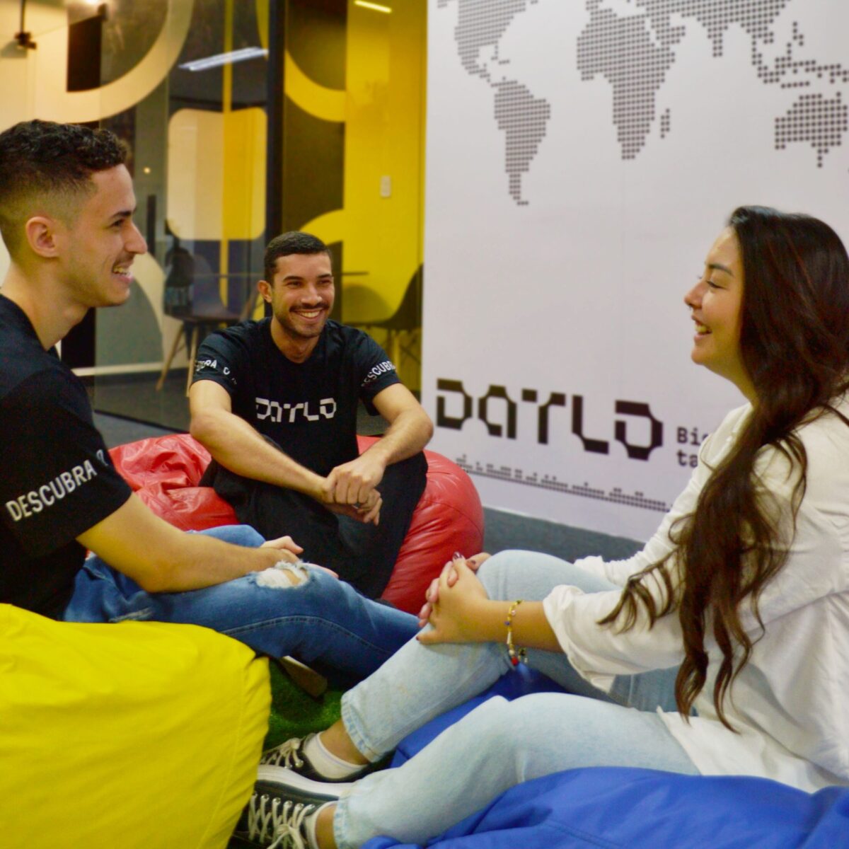 Colaboradores da Datlo sentados em pufes coloridos, conversando de forma descontraída e trocando ideias.