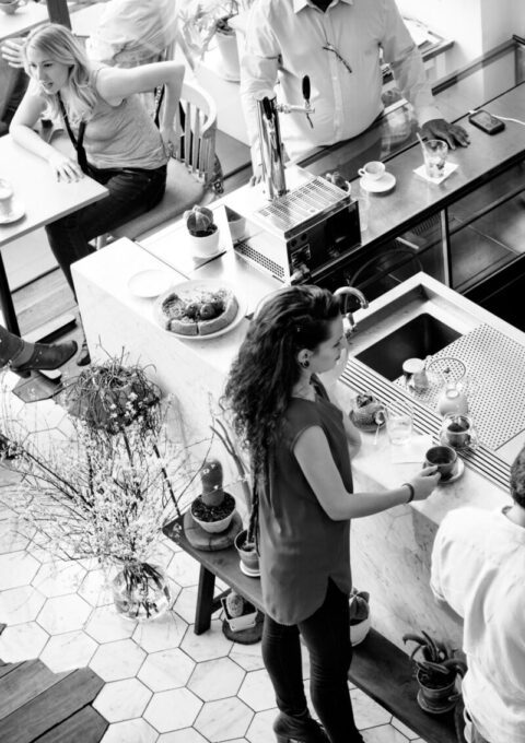 Clientes aproveitando o ambiente de uma cafeteria, enquanto atendentes trabalham no balcão.